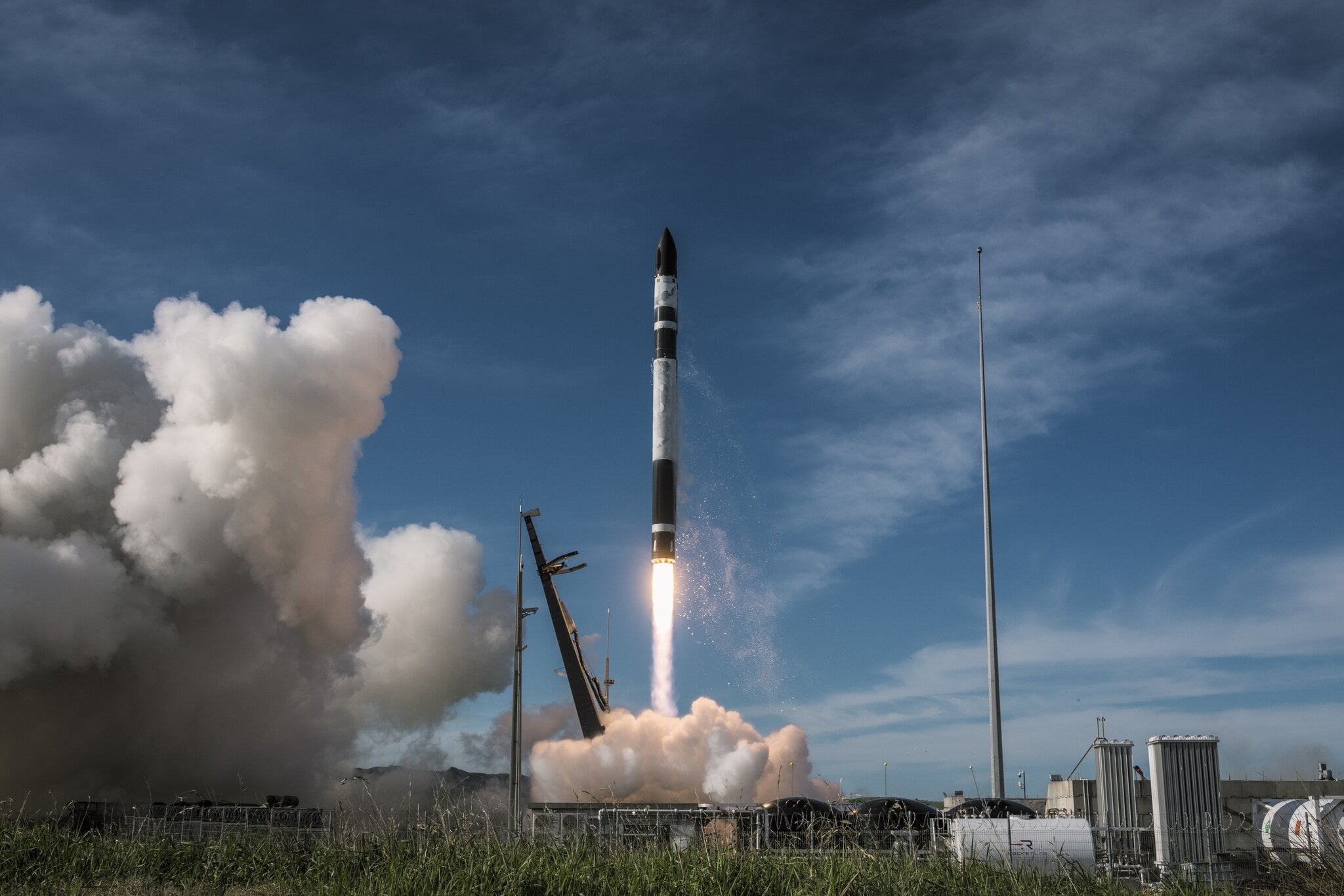 An Electron rocket lifts from the launch pad with a bright exhaust plume and drifting smoke.